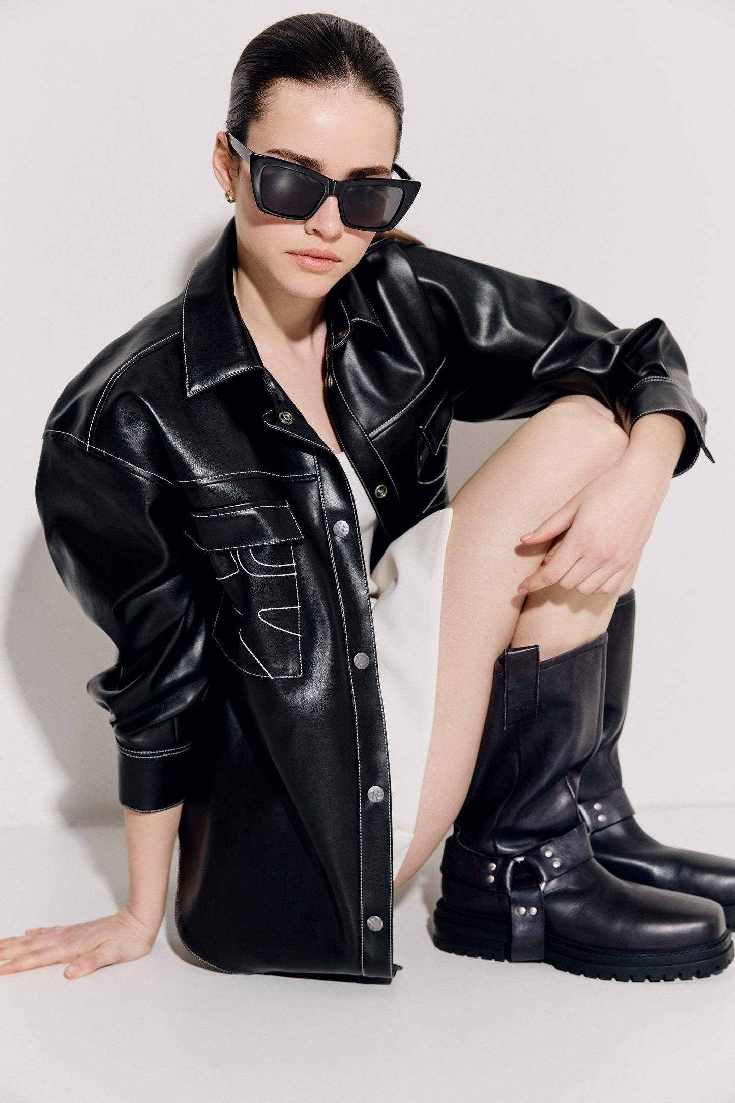 A person wearing a black leather jacket and black boots, sitting with their hands on their knees.