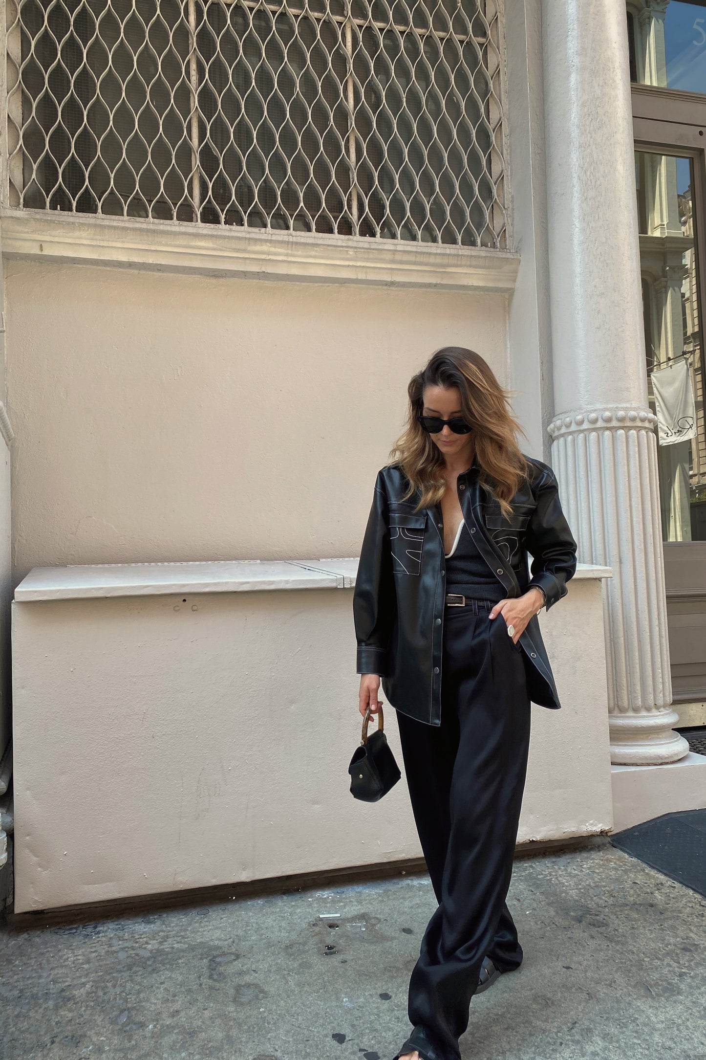 Woman in black outfit standing on a street with architectural background